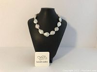 Front view of the necklace displayed on a black neck mannequin with a Lynnell Studios logo card in front.