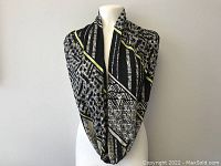 Infinity scarf displayed on a mannequin, showing geometric black, beige, and olive pattern.
