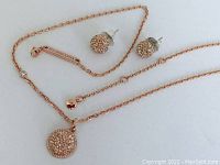 Rose gold tone pendant necklace with round crystal-encrusted pendant and matching crystal ball stud earrings displayed on a white surface.