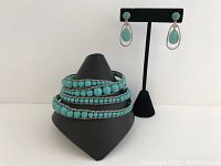 Turquoise beaded multi-wrap bracelet displayed beside the turquoise and silver drop earrings on a black stand.