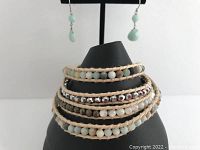 Bracelet displayed on a black stand with aqua green drop earrings hanging behind.