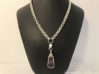 Front view of the silver-tone link chain necklace with amethyst stone pendant encased in sterling silver wire, displayed on necklace stand.