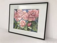 Side angled view of framed watercolour painting showing pink roses on a blue background, matted and framed in black.