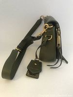 Side view showing bag depth, gold hardware, adjustable olive green leather strap with large gold clasps, and attached Marc Jacobs branded leather tags.