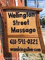 Photo of wooden sign outside Wellington Street Massage with phone number and website.