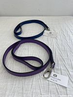 Two leather dog leashes, one purple and one blue, displayed on a white cloth background with Hartman & Rose tags attached