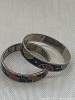 Two sterling silver inlaid band rings with colorful geometric and fruit designs, shown on white textile background.