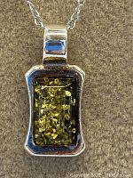 Close-up of amber stone in rectangular sterling silver pendant with visible golden inclusions.