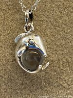 Close-up of 925 sterling silver dolphin pendant wrapping a clear crystal ball, attached to silver chain.