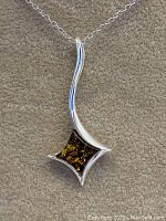 Front close-up of pendant showing green amber stone and wavy silver design on beige fabric background.