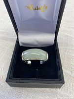 Ring on display inside black box lined with white satin, showing overall view of jade and silver band.