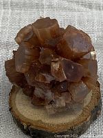 Brownish-orange aragonite crystal cluster on round wooden base, showing side and top facets of crystals.