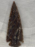 Close-up front view of the brown hand knapped Indian arrowhead showing flaked edges and color variations.