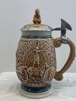 Side view of the collectible stein highlighting the handle, lid, and figurine on top of the lid.