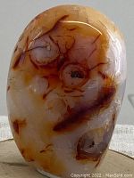 Close-up of the polished carnelian gemstone showing warm orange and reddish coloration with natural inclusions and banding.