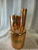 Full set of three copper canisters with brass labels for flour, pasta, and sugar, with brass handles on lids, arranged on white fabric backdrop.