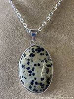 Front view of the Dalmatian Jasper pendant on chain showing oval cream-colored stone with black spots in silver setting.