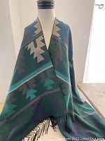 Front view of the poncho displayed on a mannequin showing the indigenous geometric pattern in blues and greens with fringed edges.