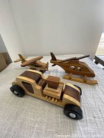 Three wooden model toys: car, biplane, and helicopter set on white cloth background showing overall condition and size comparison.