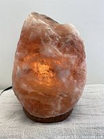 Front view of the Himalayan salt lamp showing the amber glow and rough pink salt crystal texture on a wooden base.