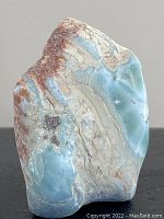 Front angled view of raw Larimar stone showing blue, white, and reddish mineral layers.