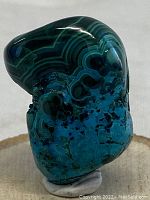 Side view of polished malachite and chrysocolla stone showing vibrant blue-green lower section with black matrix and green-black banded upper section.