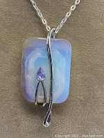 Close-up of the rectangular opalite pendant with silver detailing and purple faceted CZ stone on a silver chain