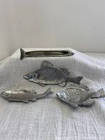 Set of three pewter fish figurines displayed on white fabric, showing scale and condition