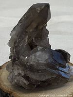 Front angle view of smoky quartz crystal cluster showing main large crystal and surrounding smaller crystals on a wood display base.