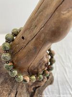 Unakite stretch bracelet displayed on wooden hand model, showing bead colors and copper spacers.