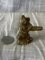 Side angle photo of small brass cat figurine playing fiddle next to a quarter for size reference.