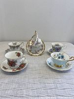 Five Royal Albert teacup and saucer sets displayed on a cloth surface showing individual floral designs and gold trimmed rims.