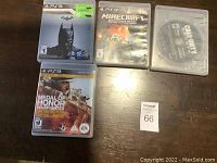 Four PS3 games included: Medal of Honor Warfighter, Call of Duty Ghosts disc, Batman Arkham City, and Minecraft, shown on wooden surface.