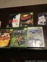 Top view of five Xbox game cases arranged on a table, clearly showing titles and cover art of Scarface, Burnout, Outlaw Golf, NHL Rivals, and Rallisport Challenge.