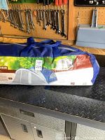 Tent packed into blue nylon carry bag with zipper and handle, showing Mountain Trails brand and label.