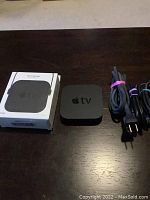 Top view of Apple TV device with cords and Multi Mount box on dark surface.