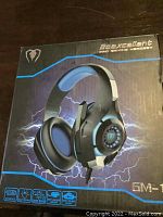 Front view of the Beexcellent GM-1 Pro Gaming Headset retail box showing the product image and key features such as USB interface, LED lights, and soft ear pads.