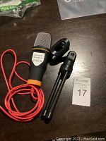 iUKUS condenser microphone with red cable shown alongside the black adjustable microphone stand with clip on a dark surface, including a MaxSold lot number card.