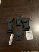 Five small pocket cutting tools in black nylon cases and one without case on dark wood surface