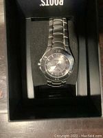 Front view of silver-tone Roots commemorative wristwatch housed in black display box.