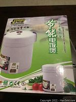 Image of the electric rice cooker in its original packaging showing the product design and box artwork with Chinese branding and product usage icons.