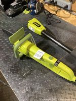 Photo of Sun Joe electric chainsaw in handheld configuration with green and black parts on a metal workbench.