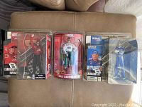 Three Dale Earnhardt Jr. NASCAR figures in original packages arranged side by side showing front view, depicting distinct racing outfits and logos for Budweiser, Oreo, and Winners Circle.