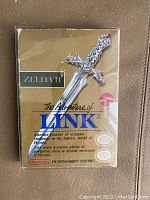 Front view of original Zelda II - The Adventure of Link gold cartridge box showing graphic of sword and game title, with visible creases and wear.