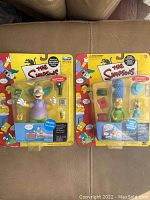 Both Krusty the Klown and Marge Simpson Playmates figures sealed in original blister card packaging showing front view, accessories visible inside.