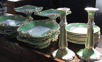 Four green and white gilt rococo-style porcelain pedestal dessert tazzas, stack of eight scalloped dessert plates, two matching candlestick holders displayed on table