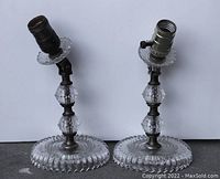 Pair of 1920s crystal bedside lamps with articulated top joints and circular pattern bases shown from front angle on white background.