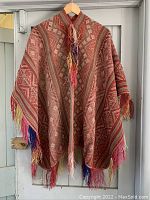 Full view of the poncho hanging on wooden hanger showing front design and fringe tassels.