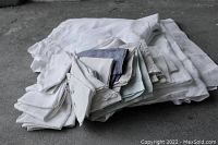 Stack of assorted white and off-white antique/vintage linens including tablecloths, napkins, handkerchiefs, showing varying textures and embroidered details.