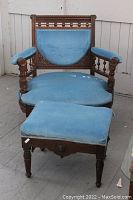 Full view of antique carved wooden chair with blue velvet upholstery and matching footstool showing overall condition and style